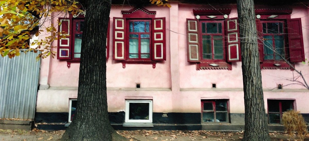 a pink house with red shutters and trees in front of it