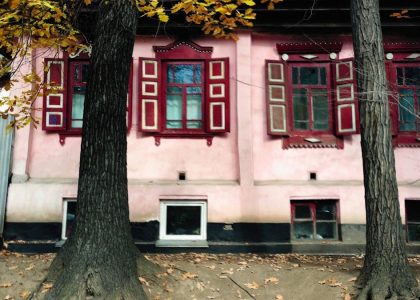 a pink house with red shutters and trees in front of it