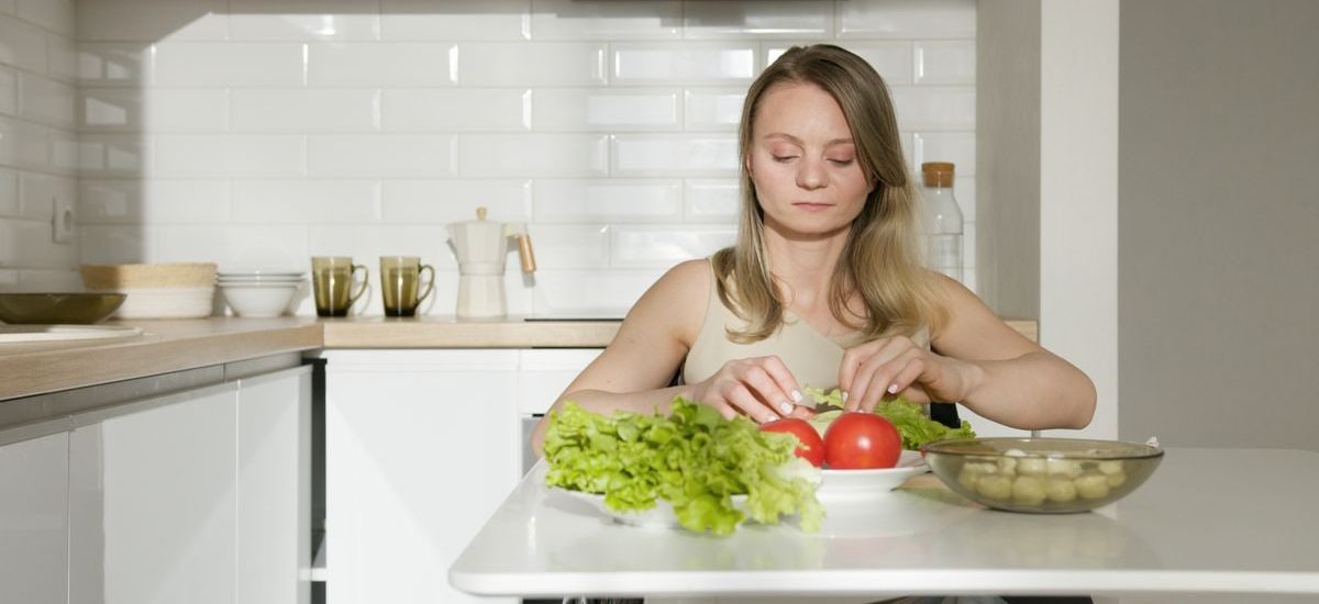 Woman sitting at table preparing fresh vegetables in a modern kitchen, highlighting healthy living and independence.